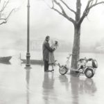 1952 man and woman holding each other next to Lambretta scooter on waterside
