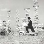 1960 man and woman with two Lambretta scooters in front of a lot of signs with cities