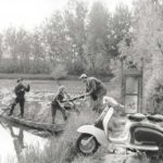 1960 man with Lambretta scooter helping two people with their boat