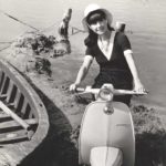 1964 woman on Lambretta scooter on the beach with boat