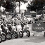 1968 six men on Lambretta scooters next to sign
